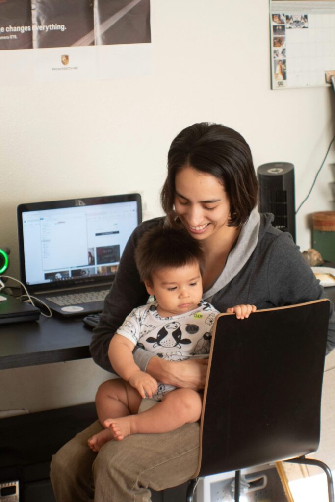 woman multitasking at home with a child on her lap and a computer. Common causes of stress in women