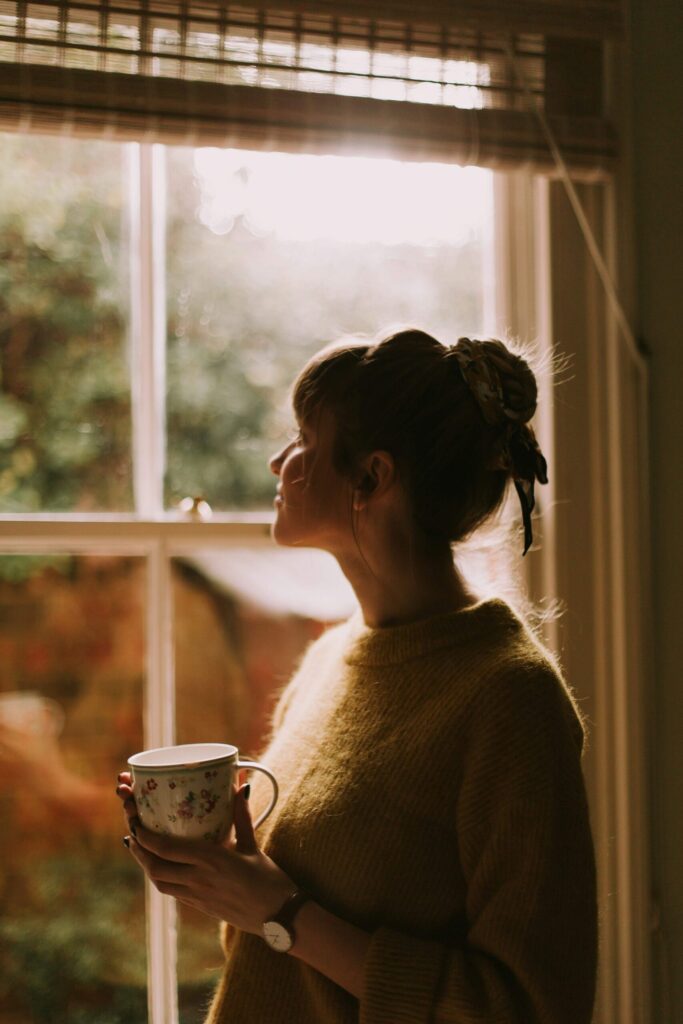 Midlife woman reflecting by a window, feeling stuck and searching for clarity